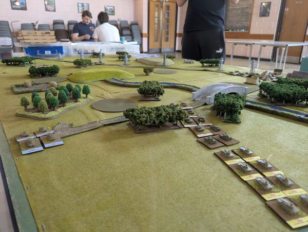 Overhead view of the full battlefield showing tank formations, wooded terrain and a bridge