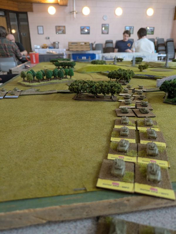 Wide view of a column of tanks advancing through wooded countryside